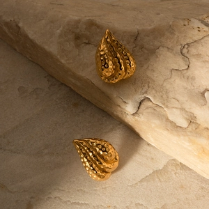 Close-up of gold drop earrings with hammered metal texture displayed on a beige stone