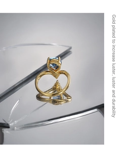 Detail of gold plated ring featuring a blue teardrop zircon on a reflective surface