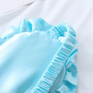 Pale blue faux silk sleep mask with ruffled edges and elasticated headband on white fabric