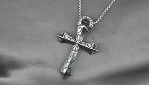 Detailed macro view of vintage engraved silver cross pendant on glossy silk background
