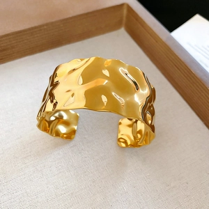 Detail of wide open cuff bracelet in gold finish with unique hammered metal texture