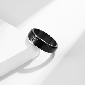 Black stainless steel spinner ring with cross engraving on a minimalist white stage