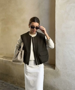 Detail of a dark olive zip-up wool vest paired with a cream outfit and bucket bag
