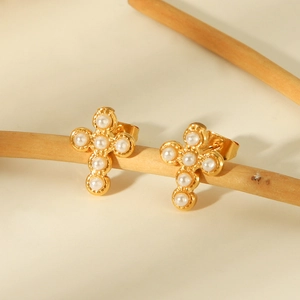 Golden stainless steel cross stud earrings with white pearls hanging on a wooden branch