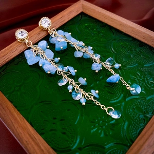 Détail de boucles d'oreilles pampilles dorées avec pierres bleues sur velours rouge