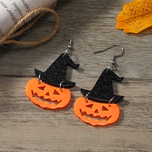 Creative Halloween pumpkin earrings with glittery black witch hats on a wooden surface
