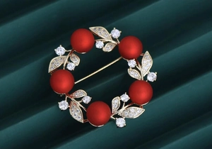 Macro shot of a wreath brooch with red frosted beads and gold leaves on green background