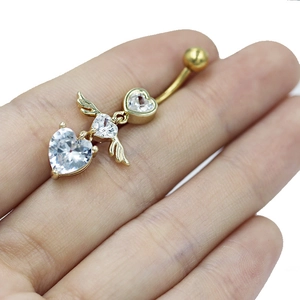 Detailed close-up of golden heart navel ring with angel wings and clear zircon in hand