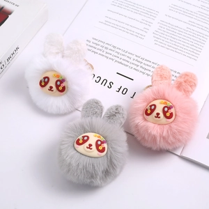 Close-up of plush bunny ear charms in white, pink and gray on a white tabletop