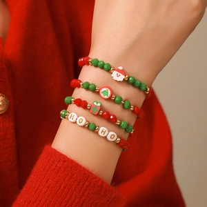 Gros plan de 4 bracelets de Noël avec breloques Père Noël sur fond de pull en tricot rouge