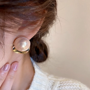 Close-up of elegant oversized pearl earring with gold metallic base on a female model