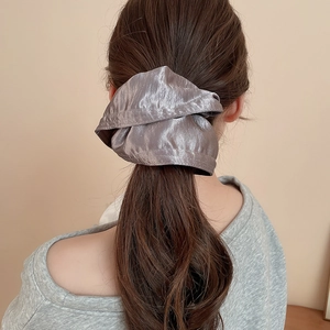 Close-up of a grey satin scrunchie with metallic sheen on a ponytail hairstyle