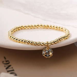 Detailed view of a gold evil eye charm bracelet draped over a white ceramic tray edge