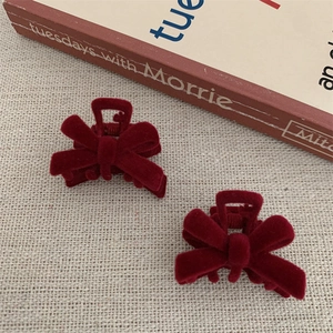 Close-up of wine red velvet bow hair clips on rustic linen background with vintage book