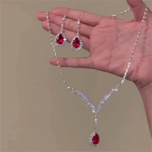 Silver necklace and earring set with red teardrop gemstones held in hand
