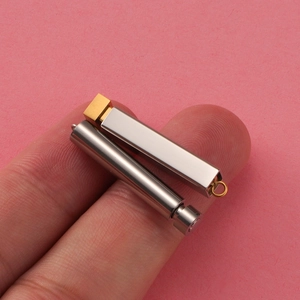 Close-up of DIY cylinder and cuboid stainless steel pendants held between fingers