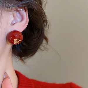 Détail de la boucle d'oreille perle rouge avec caractère chinois doré de la fortune