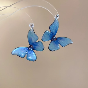 Detailed macro view of blue resin butterfly earrings with glitter and gradient wings