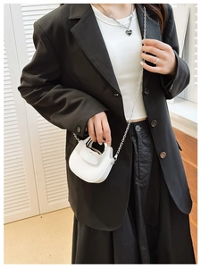 Close-up of a mini white half-moon bag with a metal chain strap on a black blazer