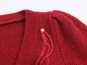 Dettaglio del cardigan in maglia rossa con bottone a perla e piume decorative fini