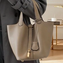 Detail of grey lychee leather bucket bag featuring a gold padlock and adjustable straps