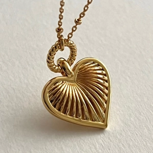Macro detail of a golden heart pendant with radial texture and spiral connector link