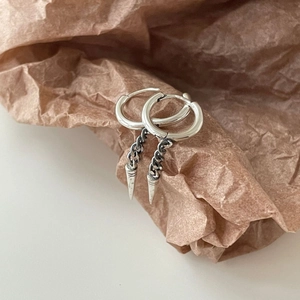 Detail of silver S925 cone rivet earrings hanging on textured paper for minimalist look