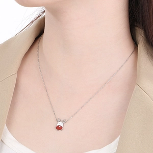 Detail view of a silver-toned reindeer necklace pendant worn by a model in a beige blazer