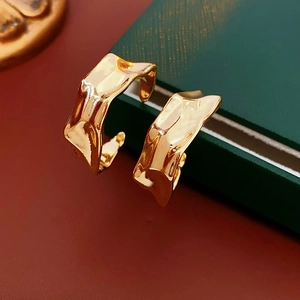 Macro view of gold irregular pleated C-shaped metal earrings on jewelry box