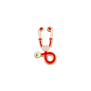 Broche stéthoscope dorée avec émail rouge et cœur rose sur un fond blanc neutre