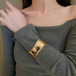 Close-up of a wide gold metal cuff bracelet with a glossy finish on a grey sweater sleeve