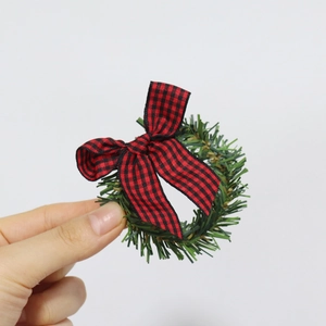 Close-up of a pine needle napkin ring with a red and black plaid bow for Christmas decor