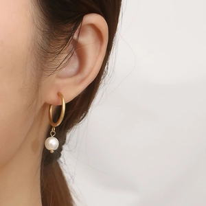 Detail of gold C-shaped earring with white pearl drop on female model ear