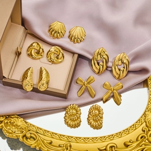 Close-up of gold-plated stud earring set featuring bow and shell textures on satin fabric
