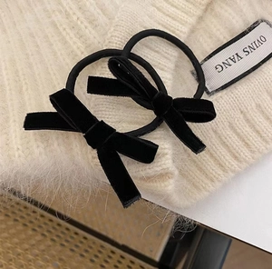 Close-up of two black velvet bow hair ties placed on a cream-colored knitted sweater