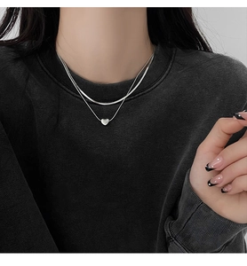 Close-up of double-layered silver heart pendant necklace on minimalist snake chain