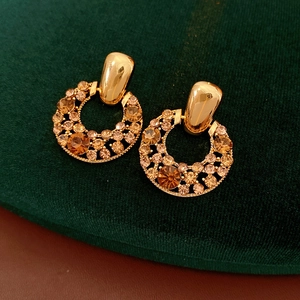 Détail de boucles d'oreilles vintage dorées avec strass champagne sur velours vert