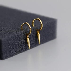 Macro shot of polished gold cone hoop earrings with spike charms on a gray display