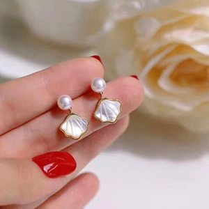 Dettaglio degli orecchini di perle a forma di conchiglia con finiture dorate tra le dita