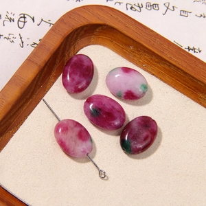 Detailed view of five oval natural gemstone beads in red and green on a wooden tray