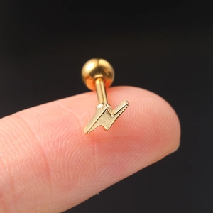 Macro shot of a tiny gold lightning bolt stud earring with ball screw back on fingertip