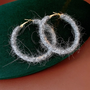 Dettaglio di orecchini a cerchio in maglia di lana grigia con chiusura in metallo dorato