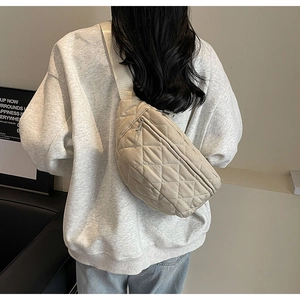 Detail view of a beige quilted crossbody bag showing texture and size on a model