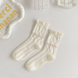 Detail of white ruffle edge socks with delicate pink floral embroidery and vertical texture