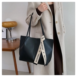 Minimalist black leather tote bag with fashion ribbon shown on model in warm interior