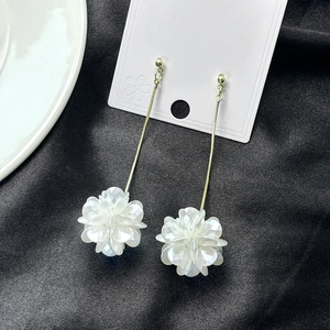 Detail of long drop earrings featuring white shell-like flowers and gold tassel chains
