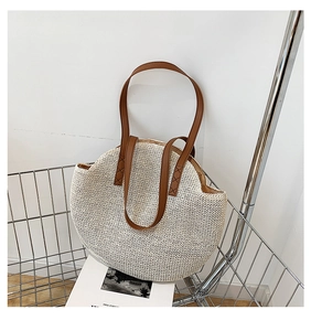 Detail of the woven texture and brown leather straps on a semi-circular straw bag