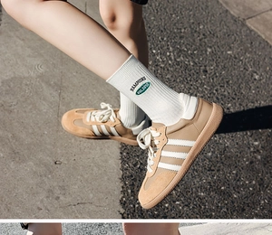 Close-up of white crew socks with green letter embroidery paired with brown suede sneakers