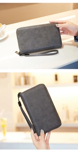 Detail of dark grey long wallet with wrist strap held in a cozy cafe setting