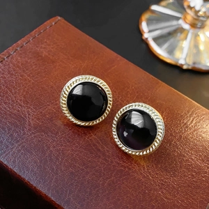 Detailed view of round black synthetic cat-eye earrings with gold braided metal border